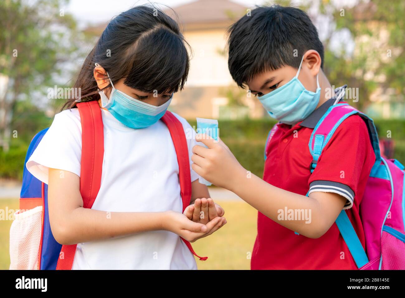 Asian boy student wear hygienic mask and press alcohol gel from bottle to hand's sister for protect  covid-19 coronavirus and epidemic virus after bac Stock Photo