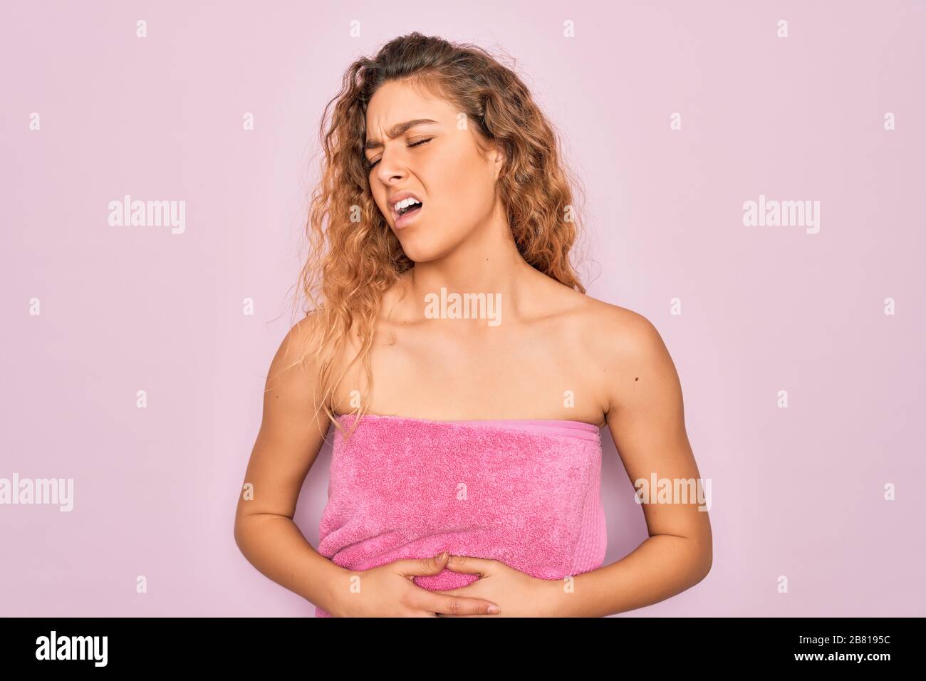 Beautiful blonde woman with blue eyes wearing towel shower after bath over pink background with hand on stomach because nausea, painful disease feelin Stock Photo