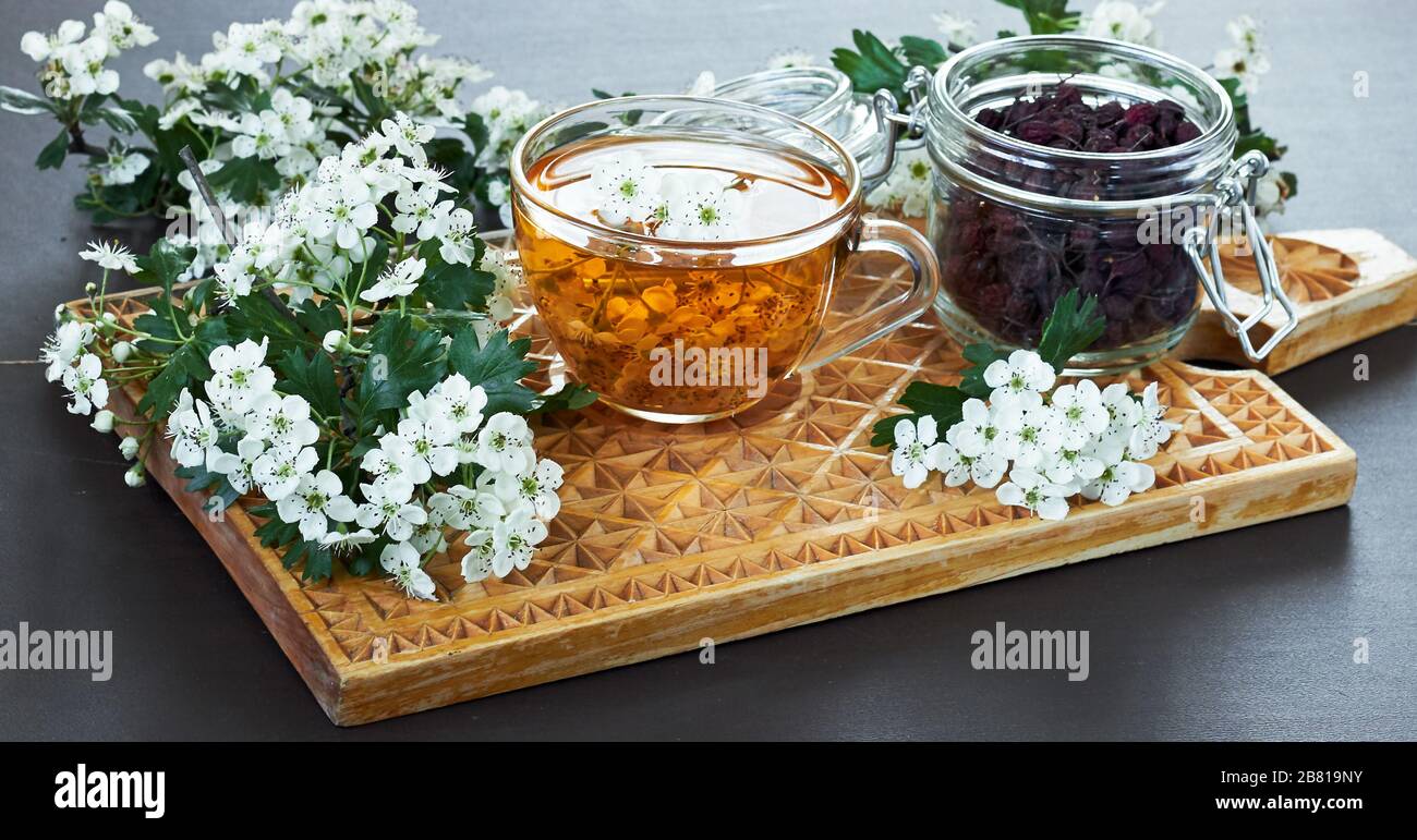 Herbal haw thorn tea from flower buds around blooming branches and a jar with berries on wooden cutting board, closeup, copy space, heart health and h Stock Photo