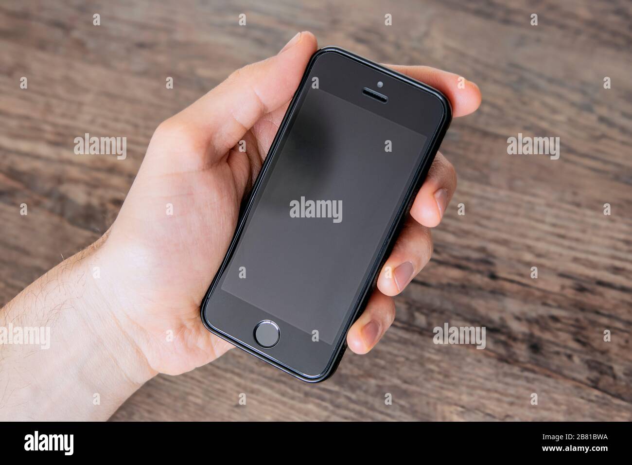 Man holding black blank phone with his left hand, close up, neutral background, view from above. Communication concept. Stock Photo
