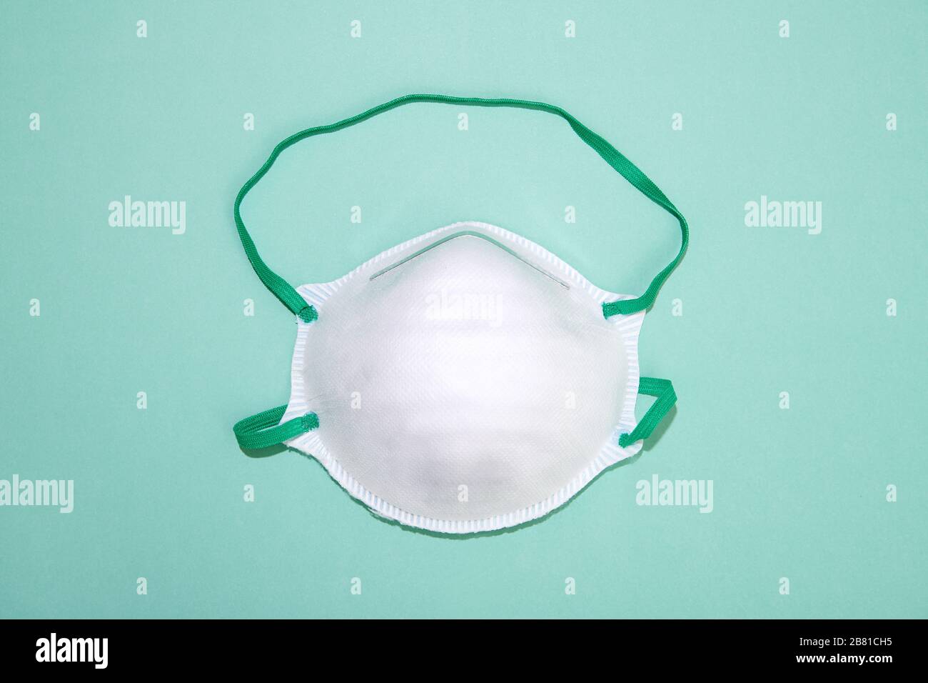 Single white coronavirus surgical face mask on green to be used as a protection from infection as well as to prevent spreading the respiratory virus Stock Photo
