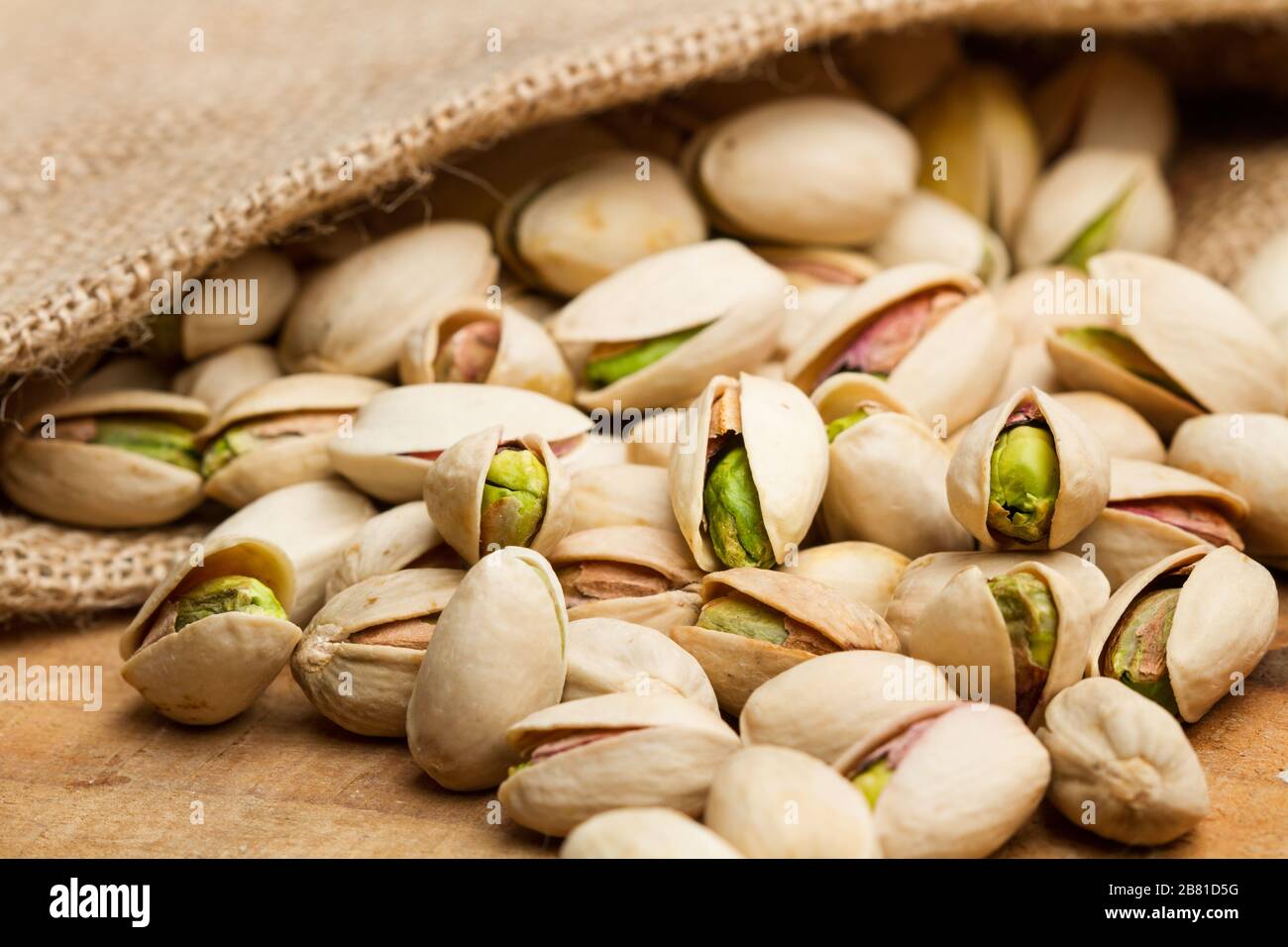 Unpeeled green pistachios in a burlap sack and on a wooden table Stock Photo
