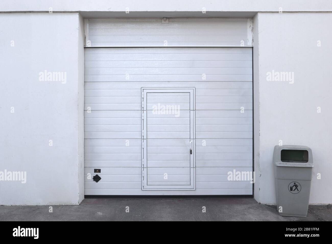 closed white garage or warehouse front with door entrance and a bin for recycling Stock Photo
