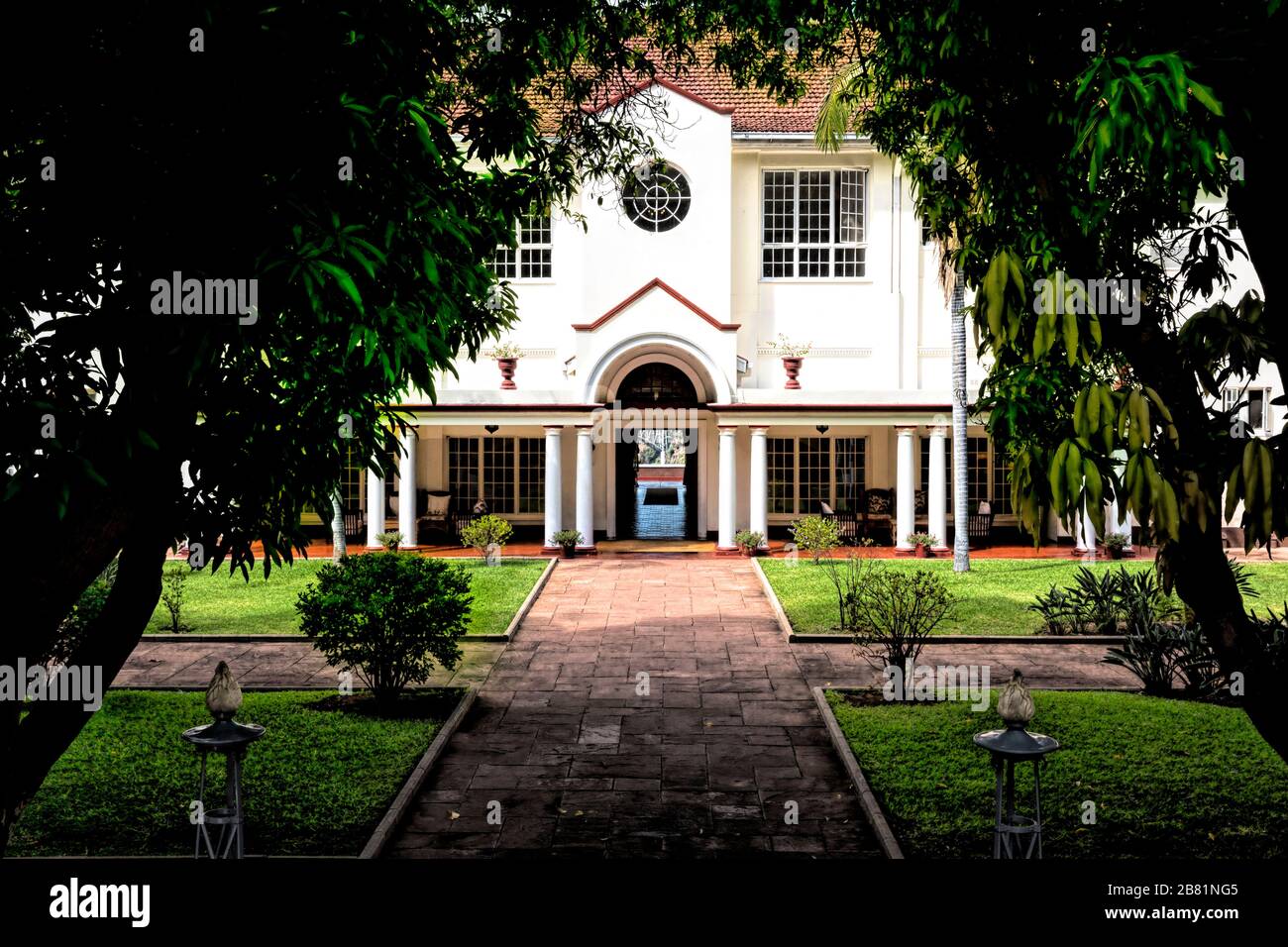 View from the formal gardens through an archway of trees to the rear entrance of Victoria Falls Hotel Stock Photo