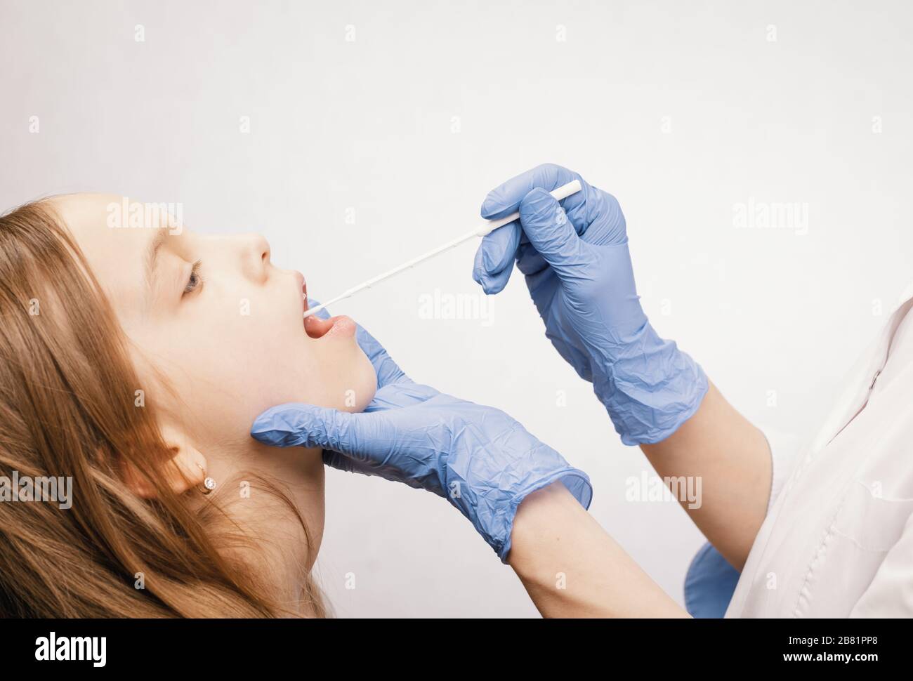 Pediatrician or doctor taking saliva test sample fom elementary age girl's lips performing Saliva testing (Salivaomics)  diagnostic procedure Stock Photo