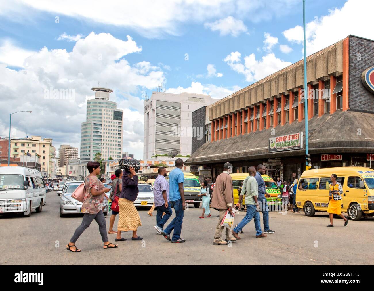 People walk in front of the traffic, across Jason Moyo Ave at its junction with Chinhoyi Street in Harare Stock Photo