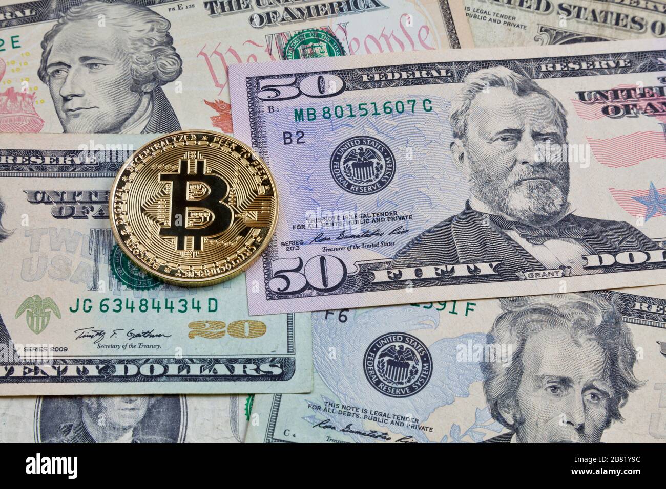 Close-up on a golden bitcoin coin on top of a stack of us dollars. Stock Photo