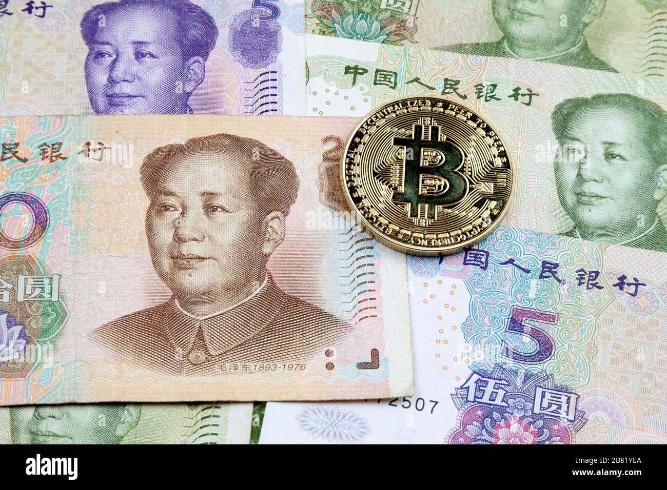 Close-up on a golden Bitcoin coin on top of a stack of Chinese Yuan banknotes. Stock Photo