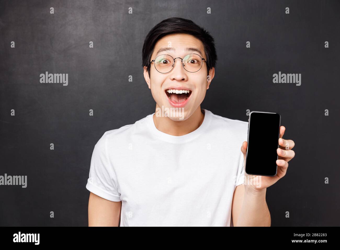 Technology, messaging and people concept. Close-up portrait of happy, surprised and impressed young excited asian man in white t-shirt, showing Stock Photo