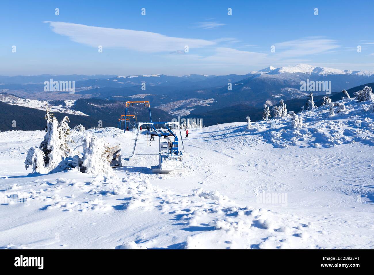 Empty ski lift covered with frost and snow with mountains at
