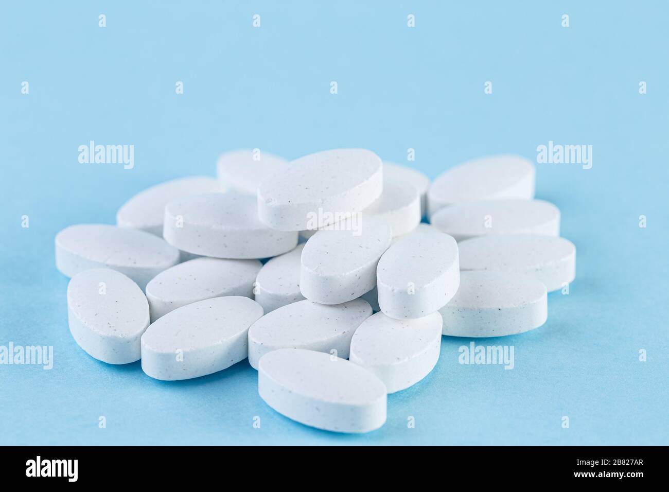 Heap of white medical pills on a light blue background. Pharmaceutical medicament, cure for health. Medicine concept. Stock Photo