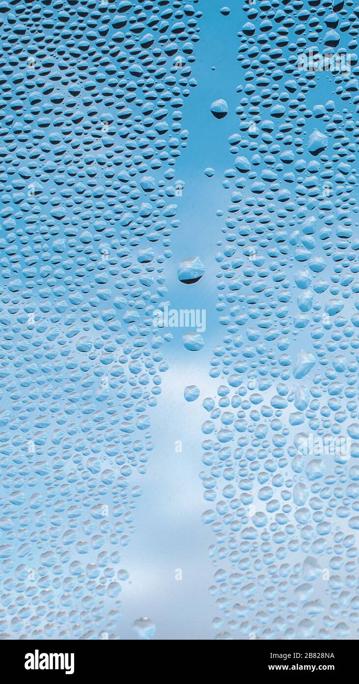 Drops water on window for mobile wallpaper design. Blue cloudy sky backdrop. Spotted abstract texture background. Spring wet weather. Droplets on glass in vertical natural cover. Fit to autumn. Stock Photo