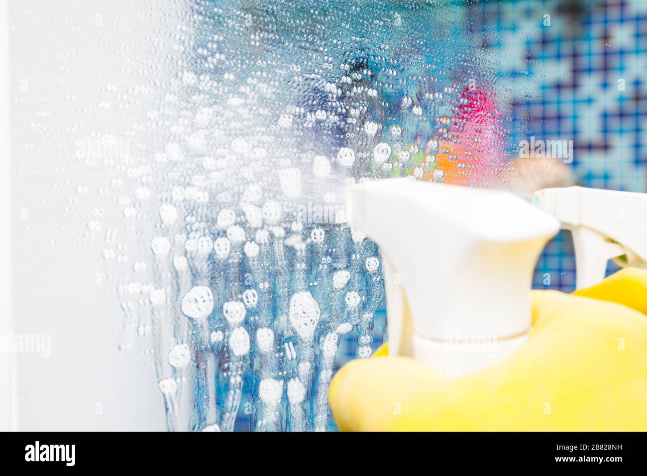 Person doing chores in bathroom at home spraying disinfectant fluid on a bathroom mirror - a protective measures against coronavirus spreading and con Stock Photo