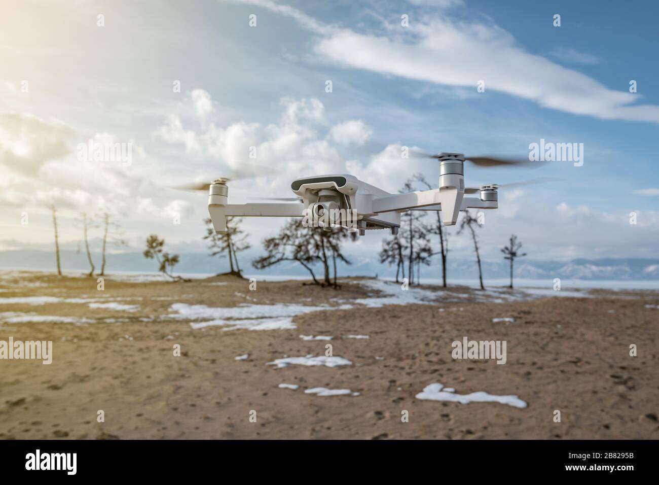 White quadrocopter drone with camera hangs in the air on the background of beautiful nature in winter. Shooting photos and videos from the air at alti Stock Photo