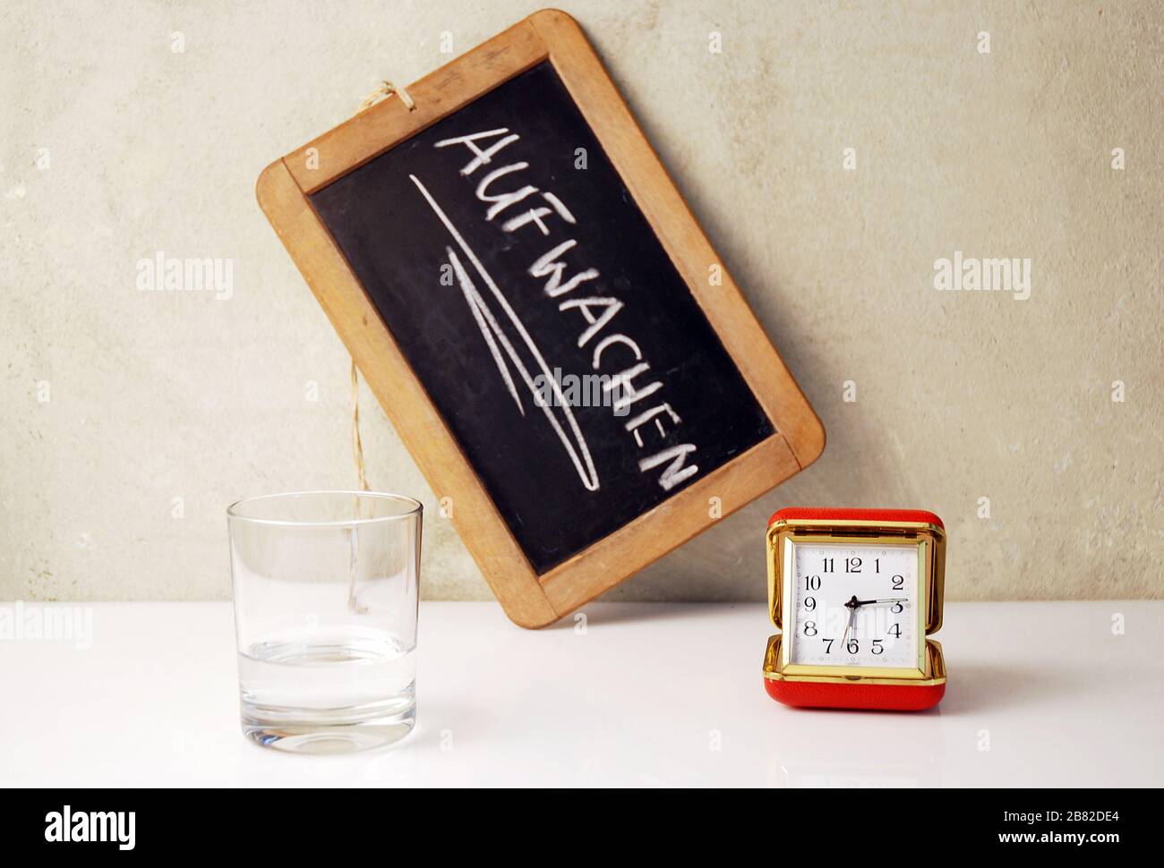 conceptual scene with a chalkboard, timer and water glas and the german text Aufwachen, translate wake up Stock Photo