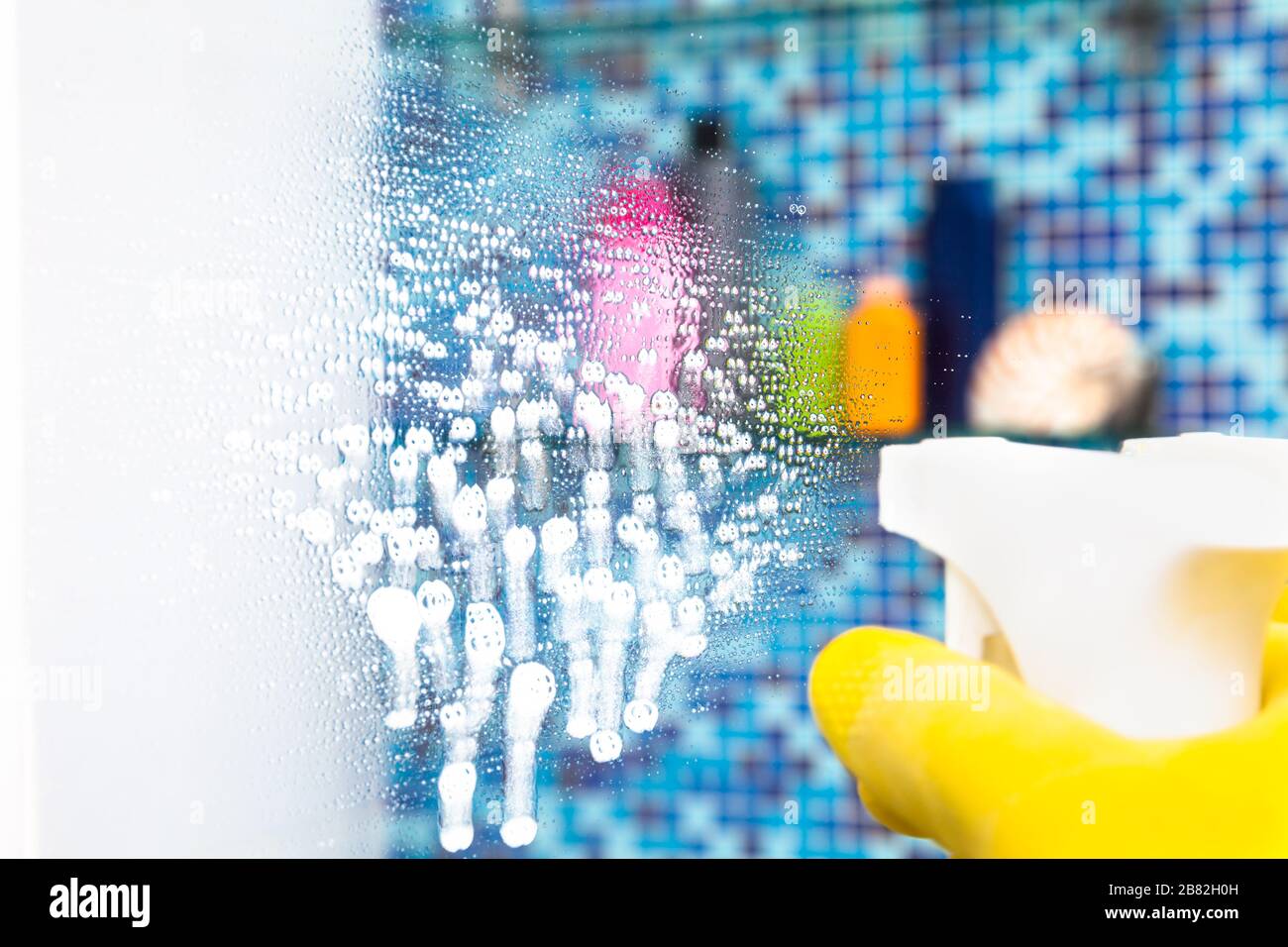 Person doing chores in bathroom at home spraying disinfectant fluid on a bathroom mirror - a protective measures against coronavirus spreading and con Stock Photo
