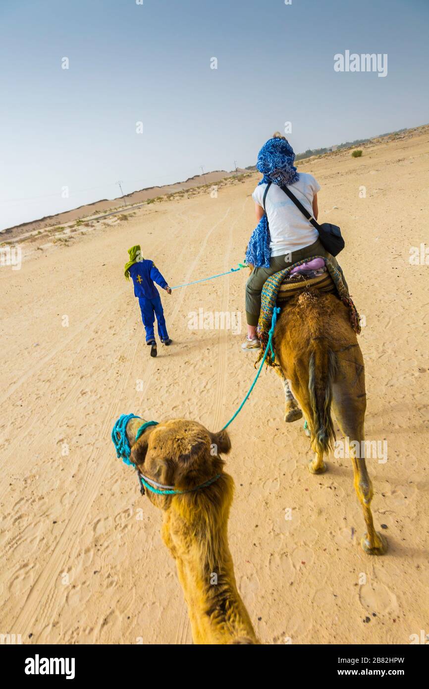 Woman and tuareg guide in a dromedary ride in the desert. Stock Photo
