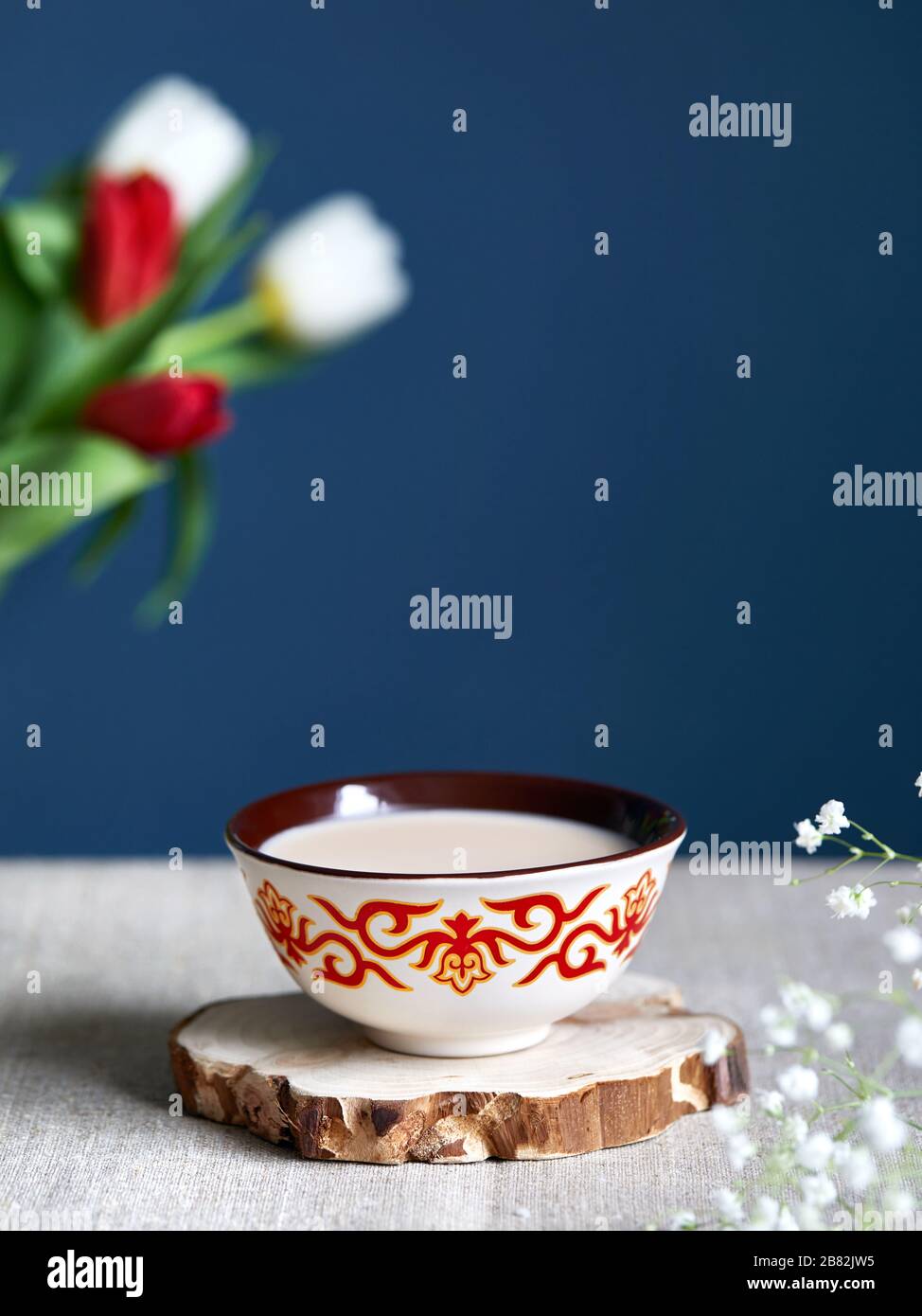 Kazakh traditional tea bowl kese with black tea and milk inside near tulips at dark blue background during Nauryz festival. Stock Photo