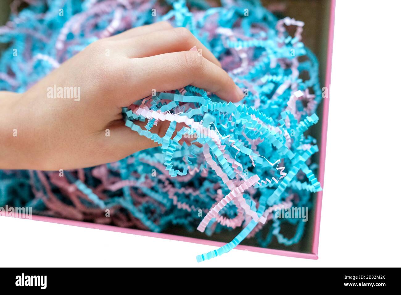 Paper shavings. Colored cut paper for packaging. Child's hand examines. Stock Photo