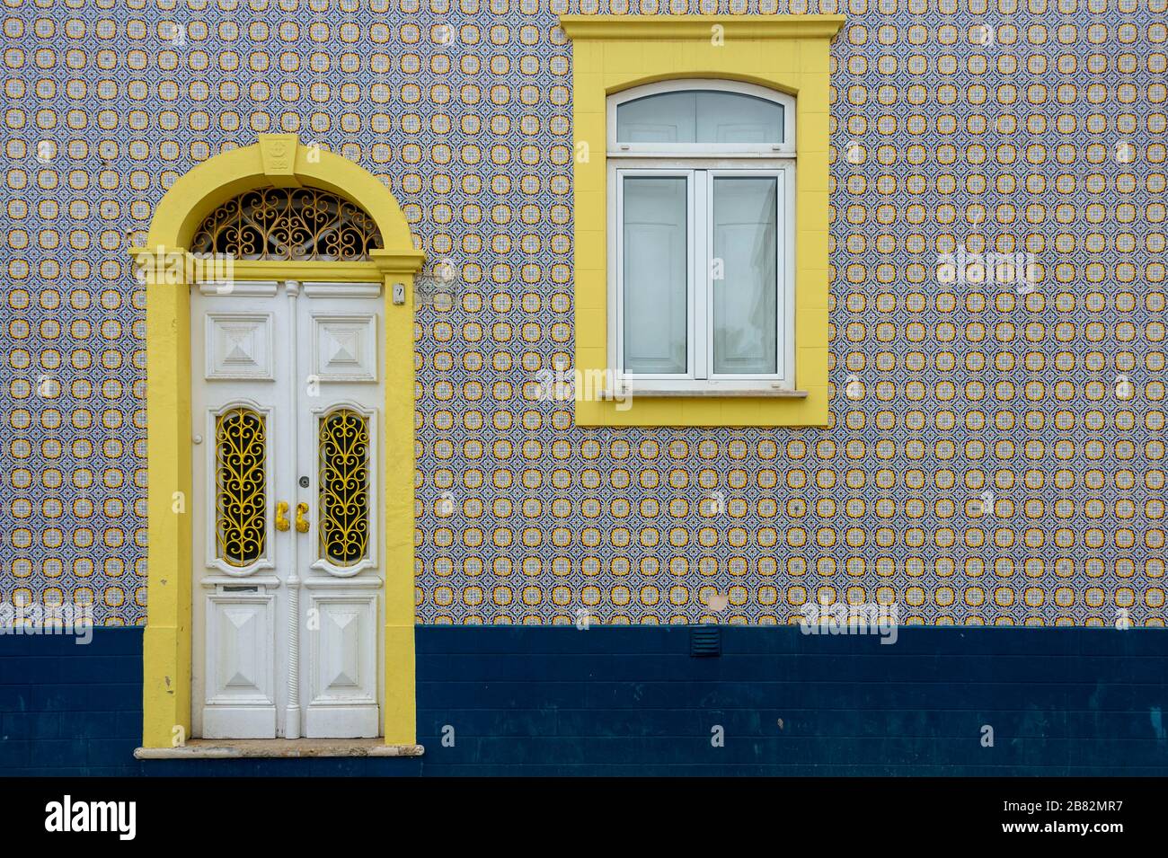 Portugal, facade of a house covered with typical ceramic azulejos tiles and a decorated wooden door in white and yellow Stock Photo