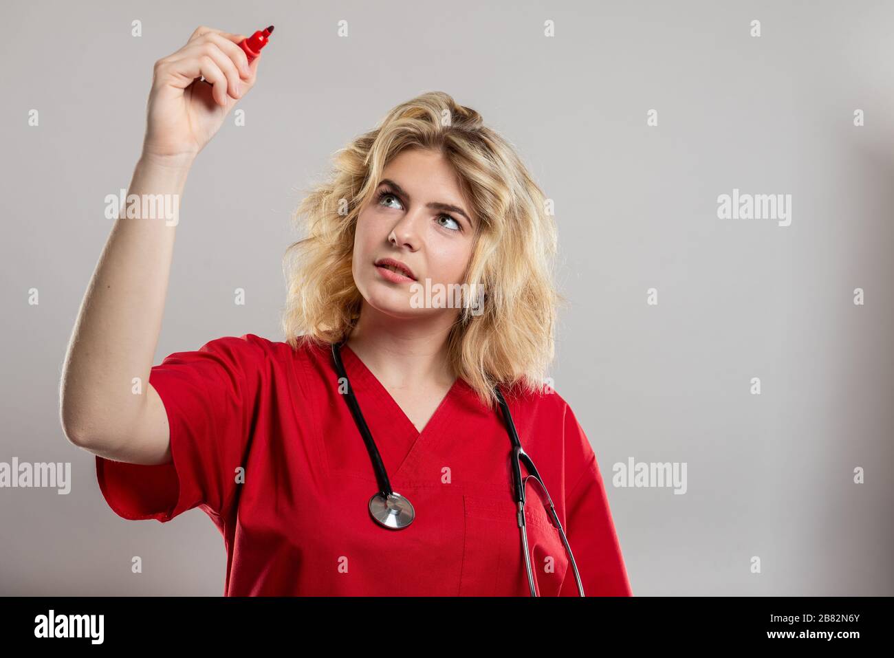 Portrait of female nurse wearing red scrub writing with marker on