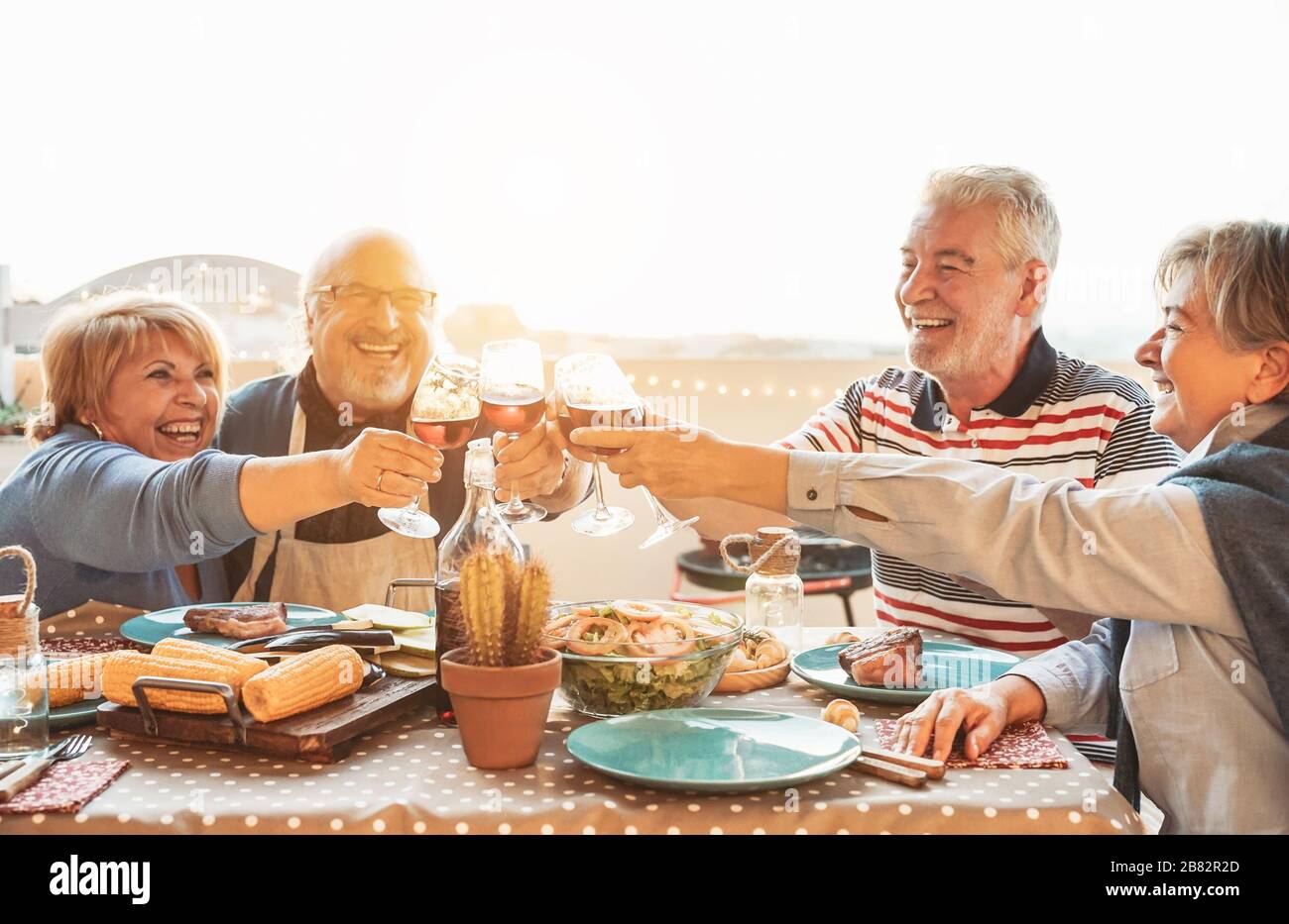 Happy senior dining and tasting red wine glasses in barbecue dinner party - Family having fun enjoying bbq at sunset time on terrace Stock Photo