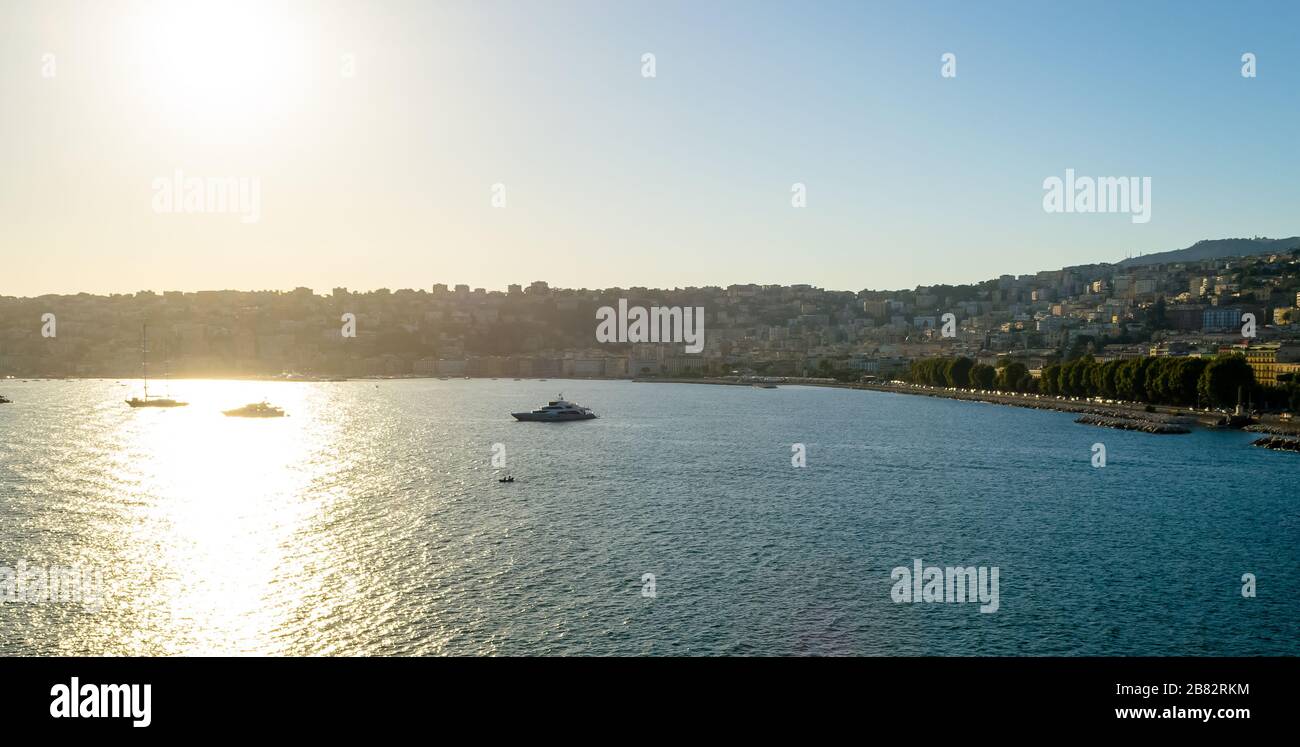 Panoramic view from the waterfront of Naples, Italy. The sunset warm light illuminating the beautiful bay and the little boats floating in the water Stock Photo