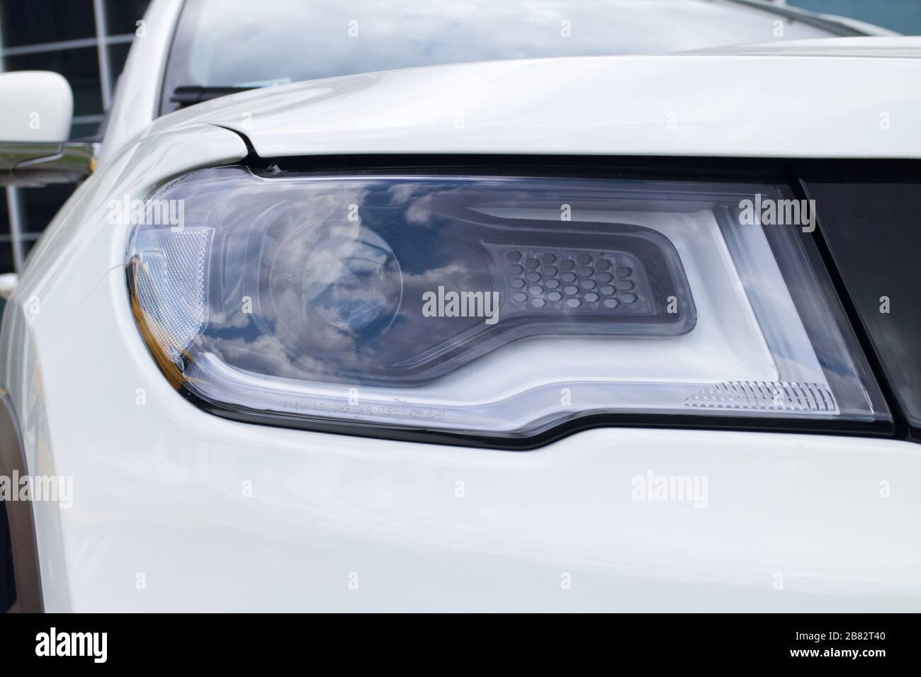 headlight on the left side of a new white car, concept of the automobile market and the automotive industry, driving lessons and obtaining a driver's Stock Photo