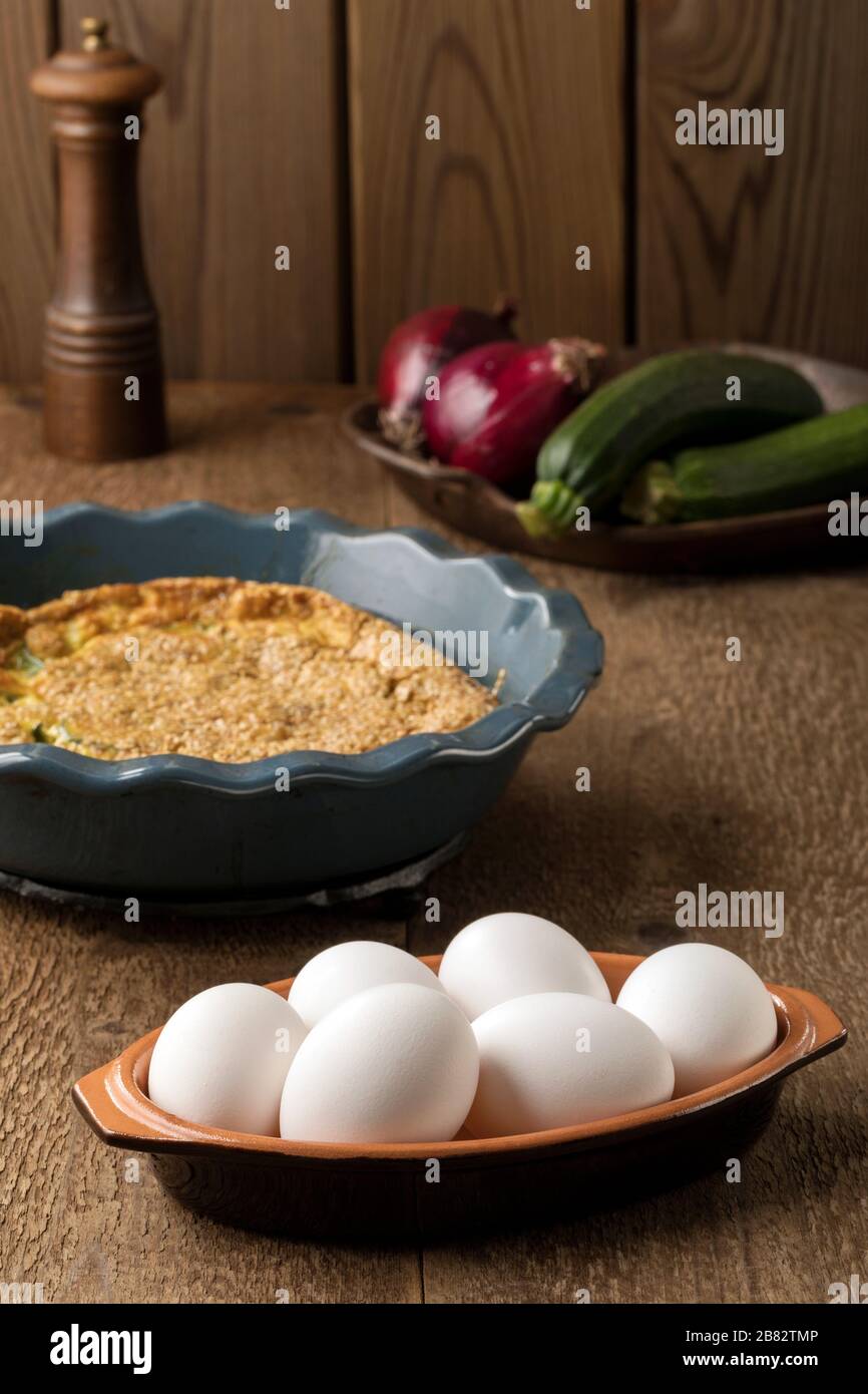 Six white eggs into a bowl and a omelette on the background on a wooden table. Stock Photo
