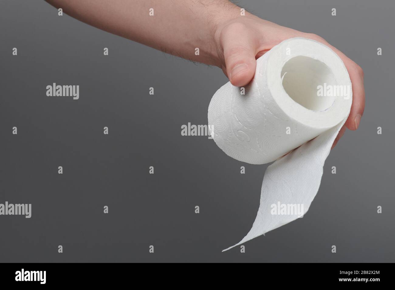 Hand hold small roll of toilet paper on gray background Stock Photo
