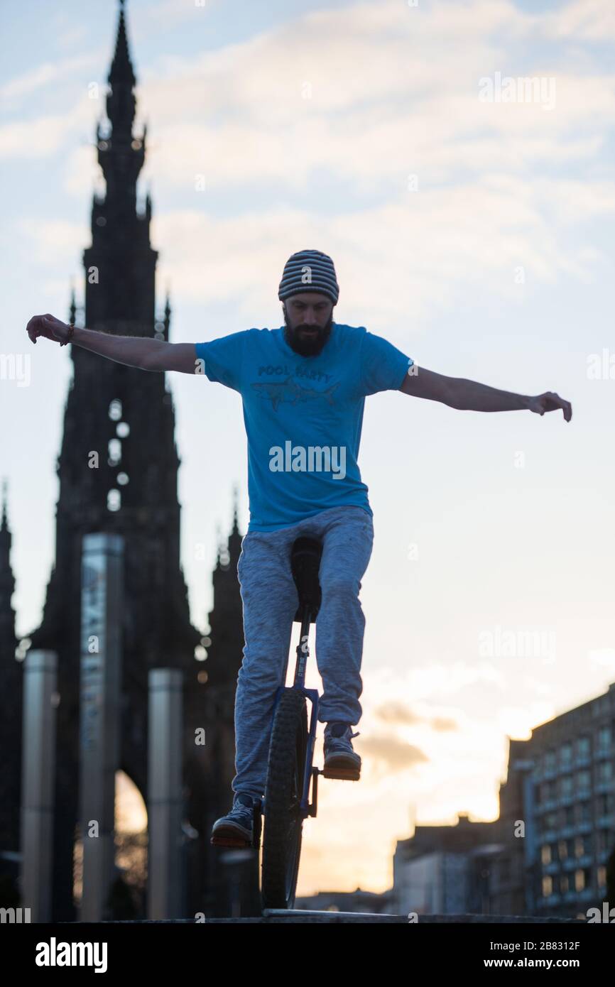 Edinburgh, UK. 19th Mar, 2020. Pictured: Andrew Buchan, a stunt and extreme unicyclist passes the time during what would normally be a busy rush hour in Edinburgh, but due to the Coronavirus pandemic the city centre is extremely quiet. People are now faced with doing different things with their time during self isolation. The Scott Monument is seen in the background which is a major landmark in Edinburgh. Credit: Colin Fisher/Alamy Live News Stock Photo