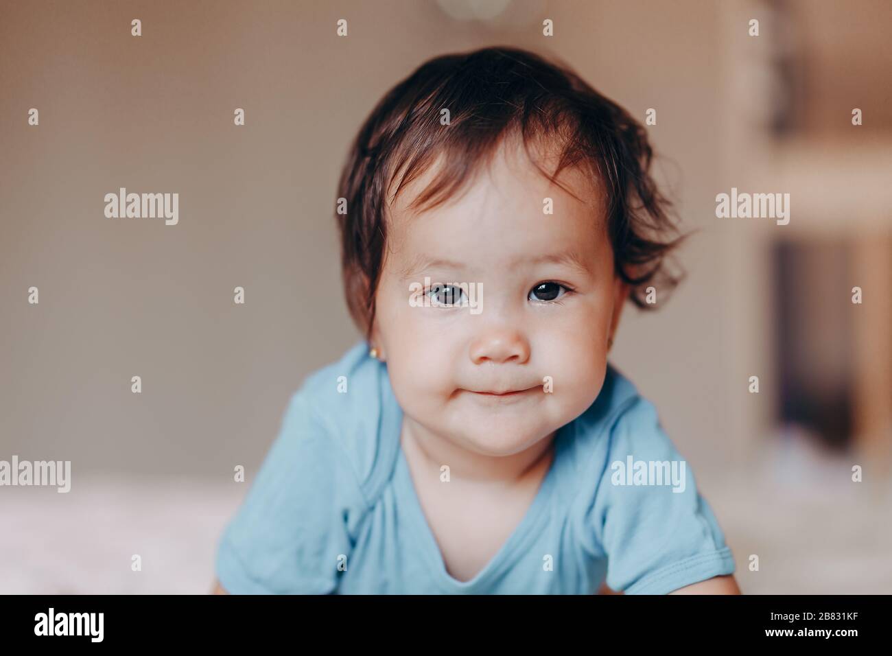 cute laughing one year old girl lying on bed and looking at camera