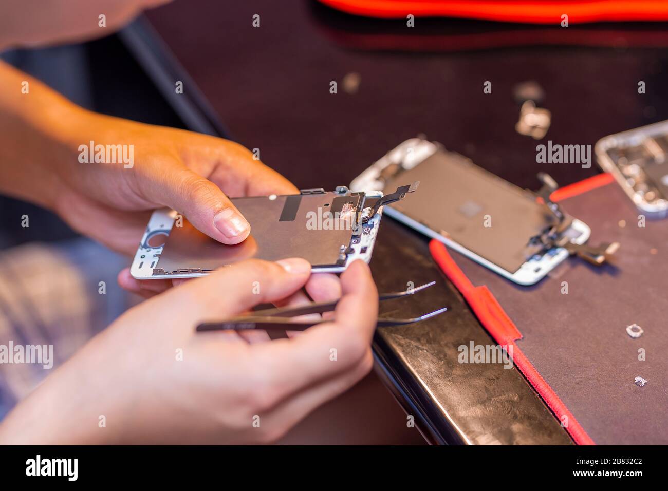 A man is repairing a mobile phone. In the frame, his hands and details of the device. repair shop for gadgets Stock Photo