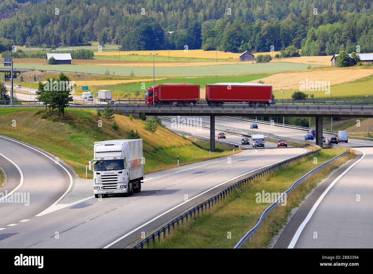 Motorway landscape with white lorry on road and red truck pulling trailer on the bridge. Salo, Finland. July 19, 2019. Stock Photo