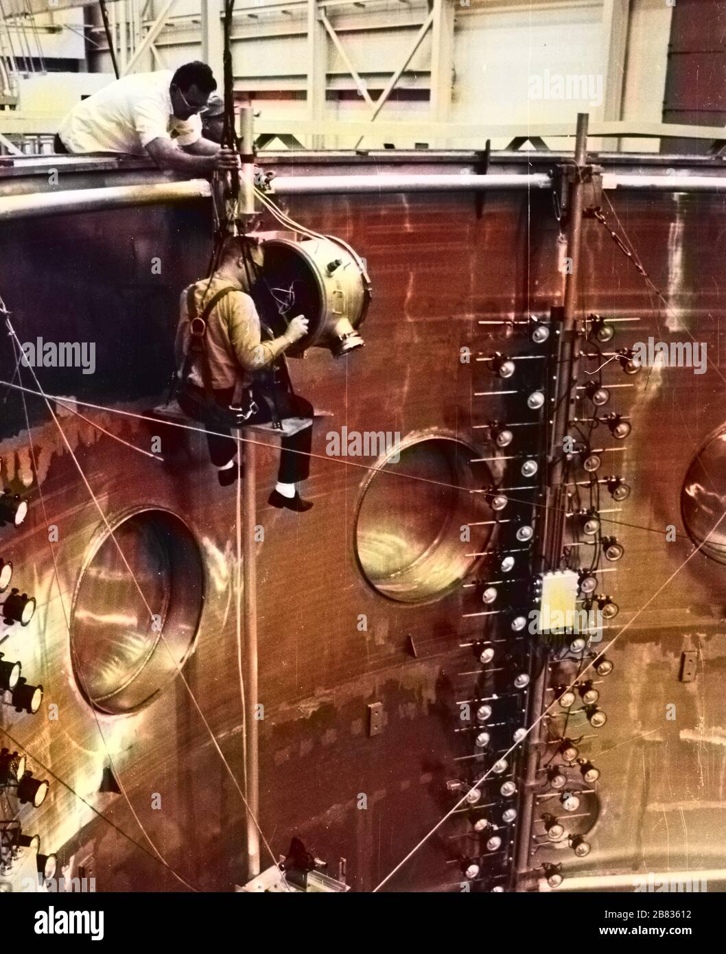 NASA photographers assembling a camera system inside the dynamic test chamber at the Goddard Space Flight Center, Greenbelt, Maryland, 1964. Image courtesy National Aeronautics and Space Administration (NASA). Note: Image has been digitally colorized using a modern process. Colors may not be period-accurate. () Stock Photo
