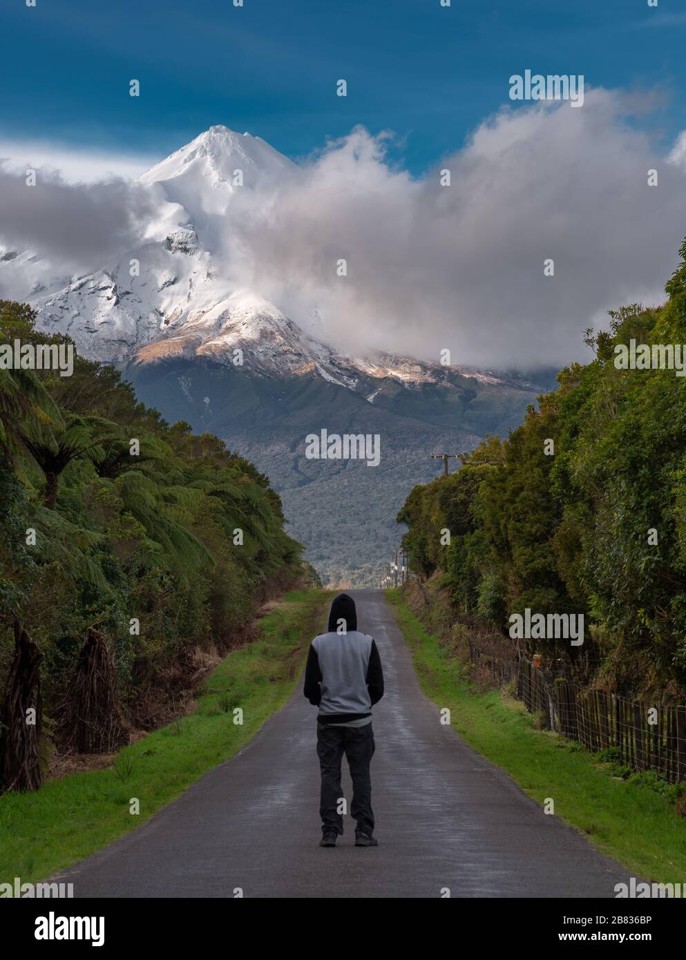 Person looking along a road towards a snow capped mountain. Mount Taranaki, New Zealand. Stock Photo
