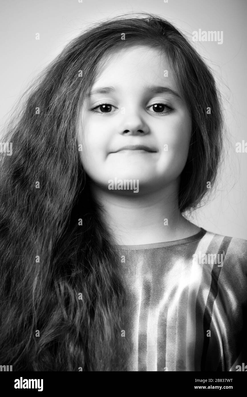 Portrait of small positive girl with long brown hair over dar grey background. Fashion and beauty concept Stock Photo