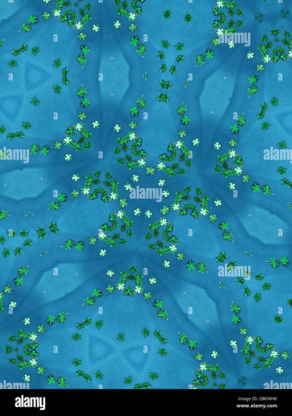 Reflective view of kaleidoscope of green clover confetti centre on sky blue background. Stock Photo