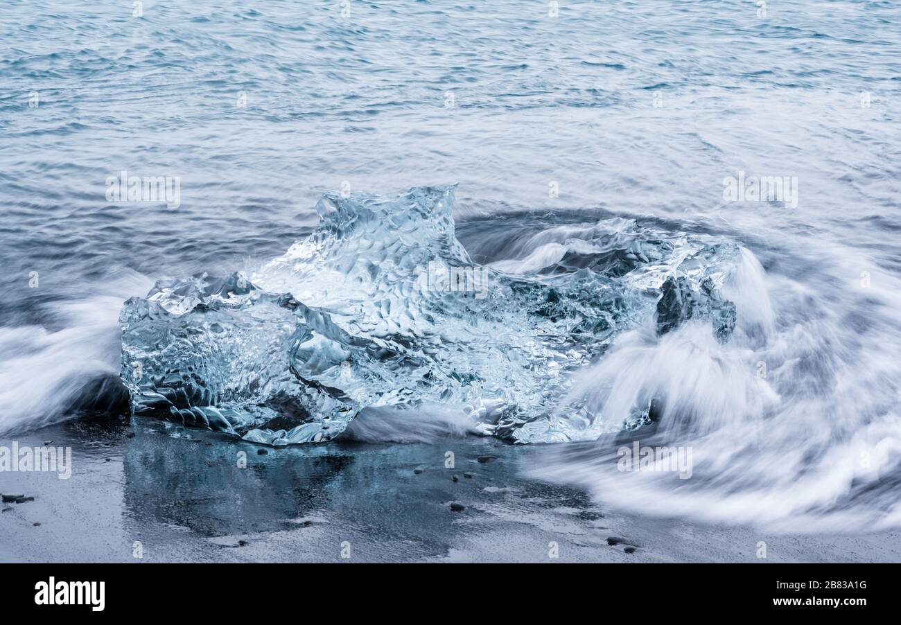 The Ocean engulfing an iceberg on Jökulsárlón. Stock Photo