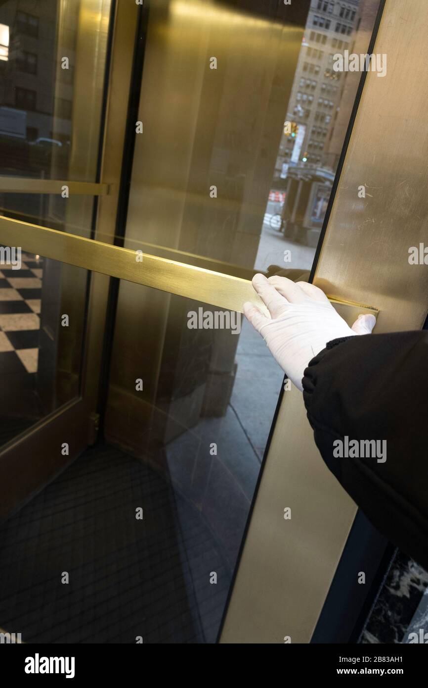 A New York City resident pushes a revolving door with a gloved hand as a precaution against germs during the COVID-19 Pandemic, USA Stock Photo