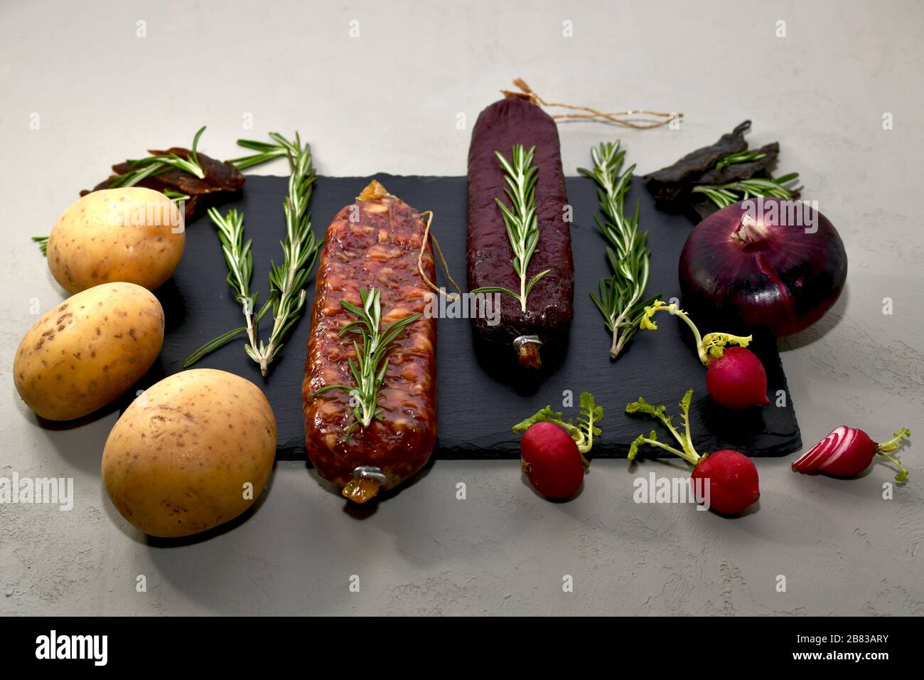 Smoked smoked meat with rosemary and vegetables on a black slate on a gray background, front view at an angle. Stock Photo