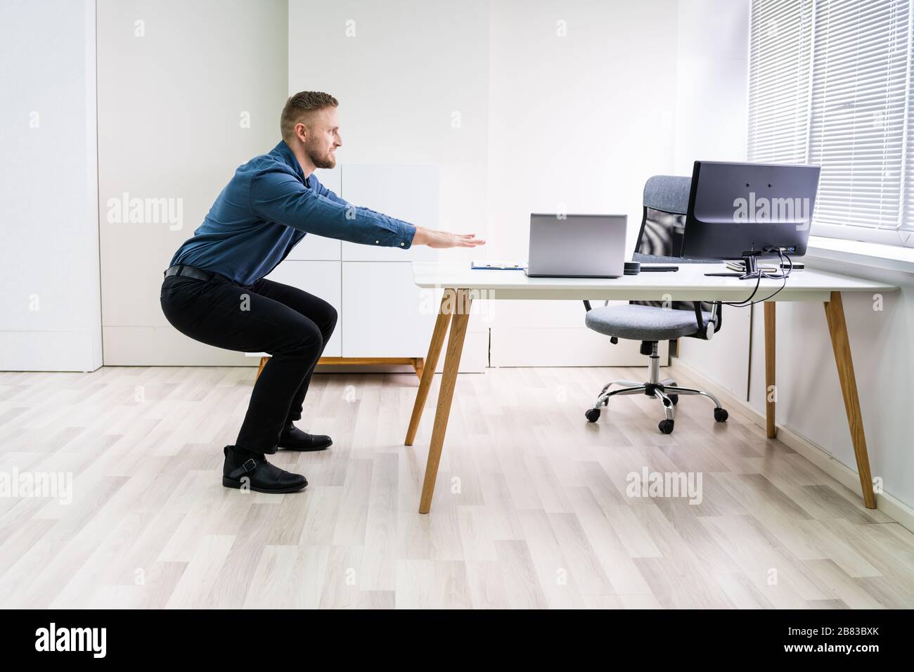 Smiling Young Businessman Doing Sit-ups At Workplace Stock Photo