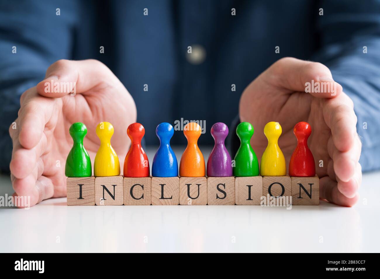 Man Protecting Inclusion Text And Multi Colored Pawns Stock Photo