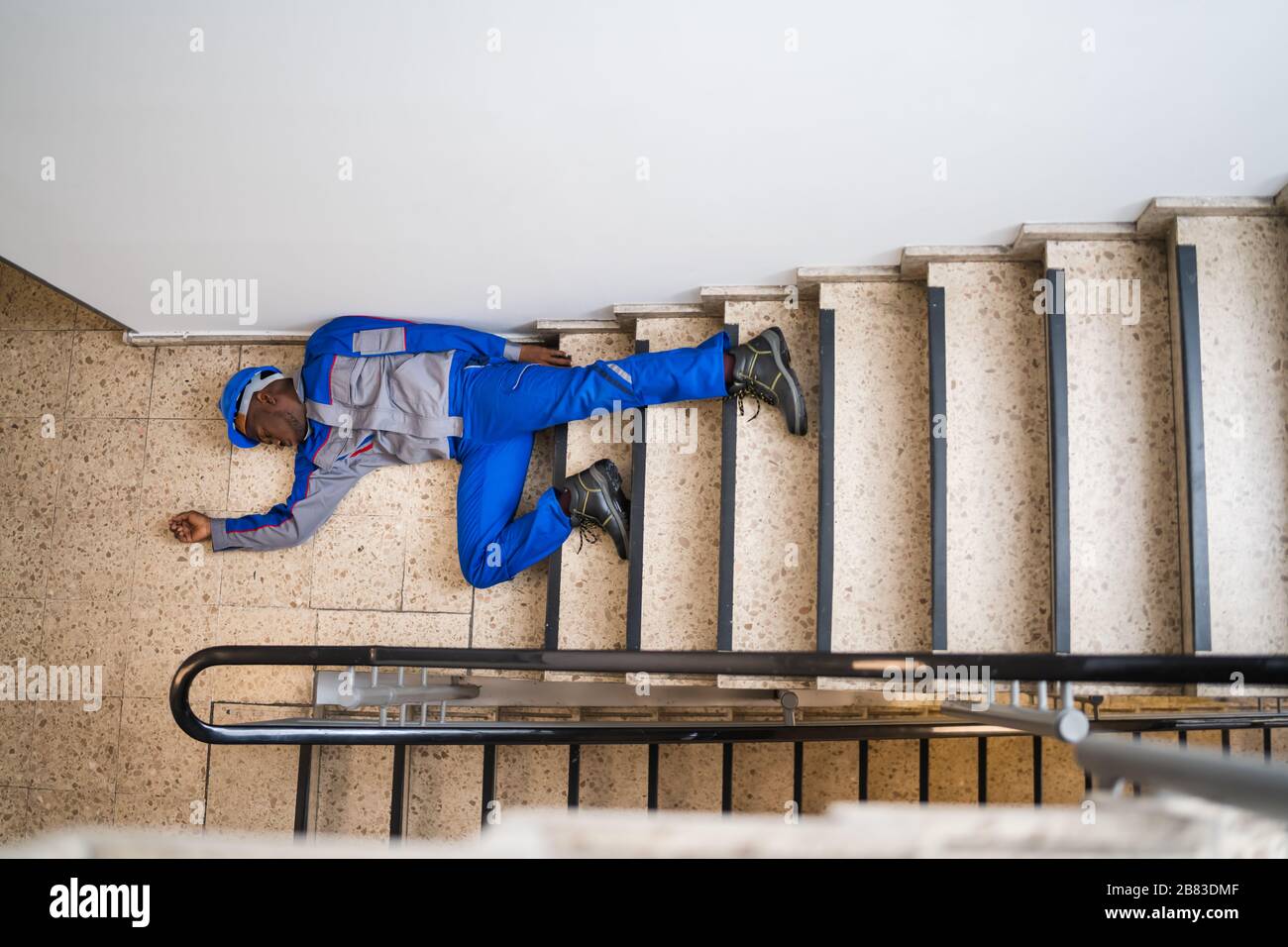 Unconscious Handyman Lying On Staircase With Helmet On Floor Stock Photo