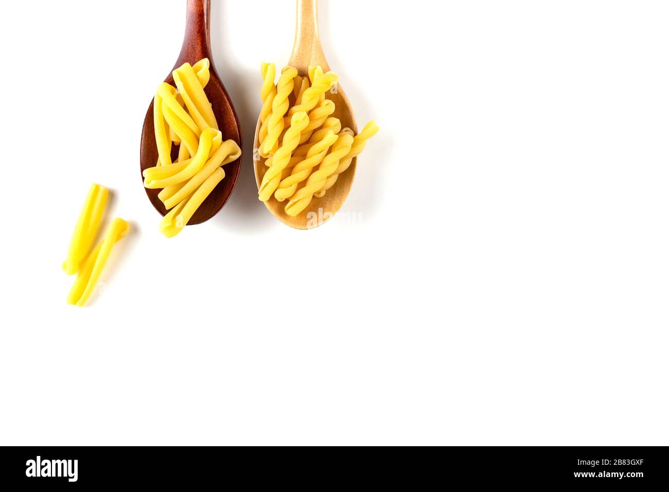 Two types of italian pasta concept. Raw gemelli, casarecce in wooden spoons on white background. Top view, copy space. Stock Photo