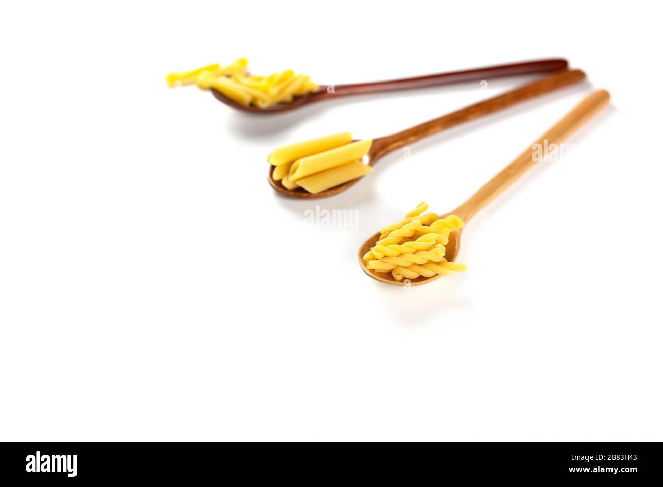 Various types of italian pasta concept. Raw gemelli, penne, casarecce in wooden spoons on white background. Copy space. Stock Photo