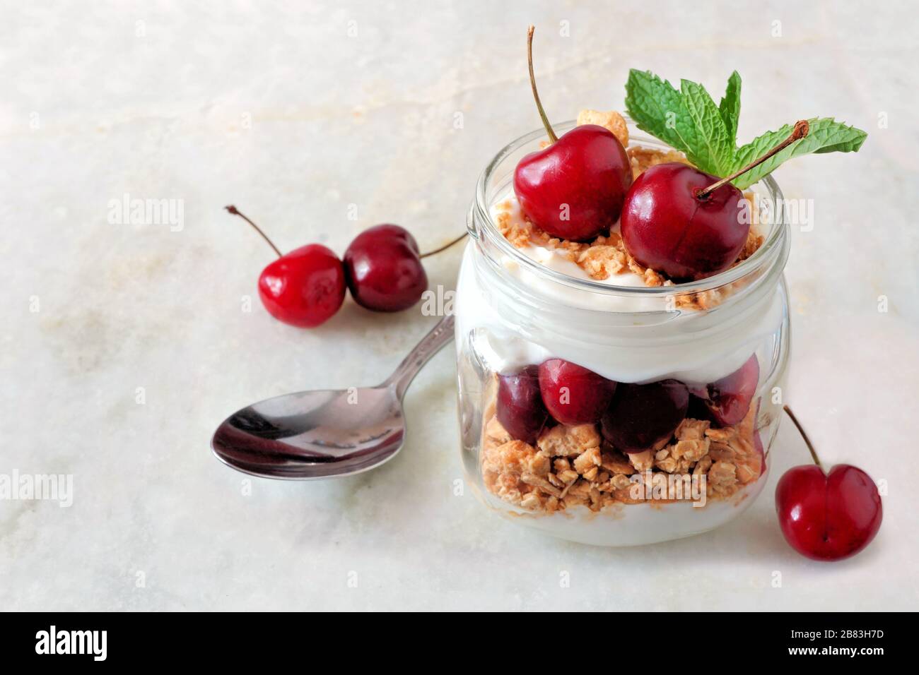 Healthy cherry yogurt parfait in a mason jar on a white marble background Stock Photo