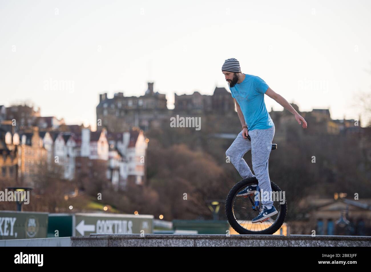 Edinburgh, UK. 19th Mar, 2020. Pictured: Andrew Buchan, a stunt and extreme unicyclist passes the time during what would normally be a busy rush hour in Edinburgh, but due to the Coronavirus pandemic the city centre is extremely quiet. People are now faced with doing different things with their time during self isolation. The Scott Monument is seen in the background which is a major landmark in Edinburgh. Credit: Colin Fisher/Alamy Live News Stock Photo