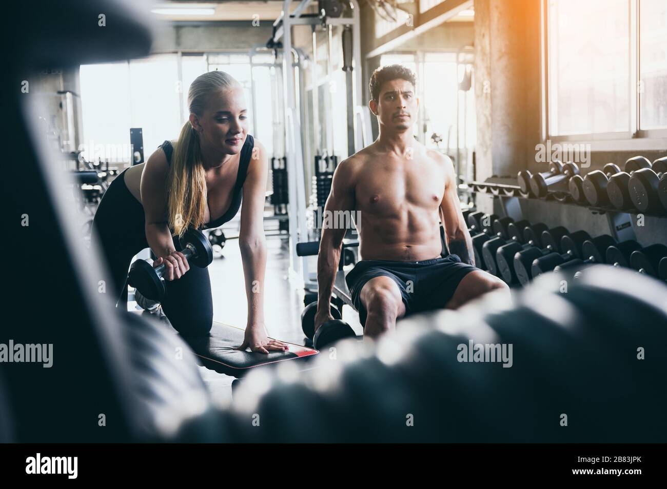 Trainer helping fit woman to lift the barbell in gym Stock Photo - Alamy