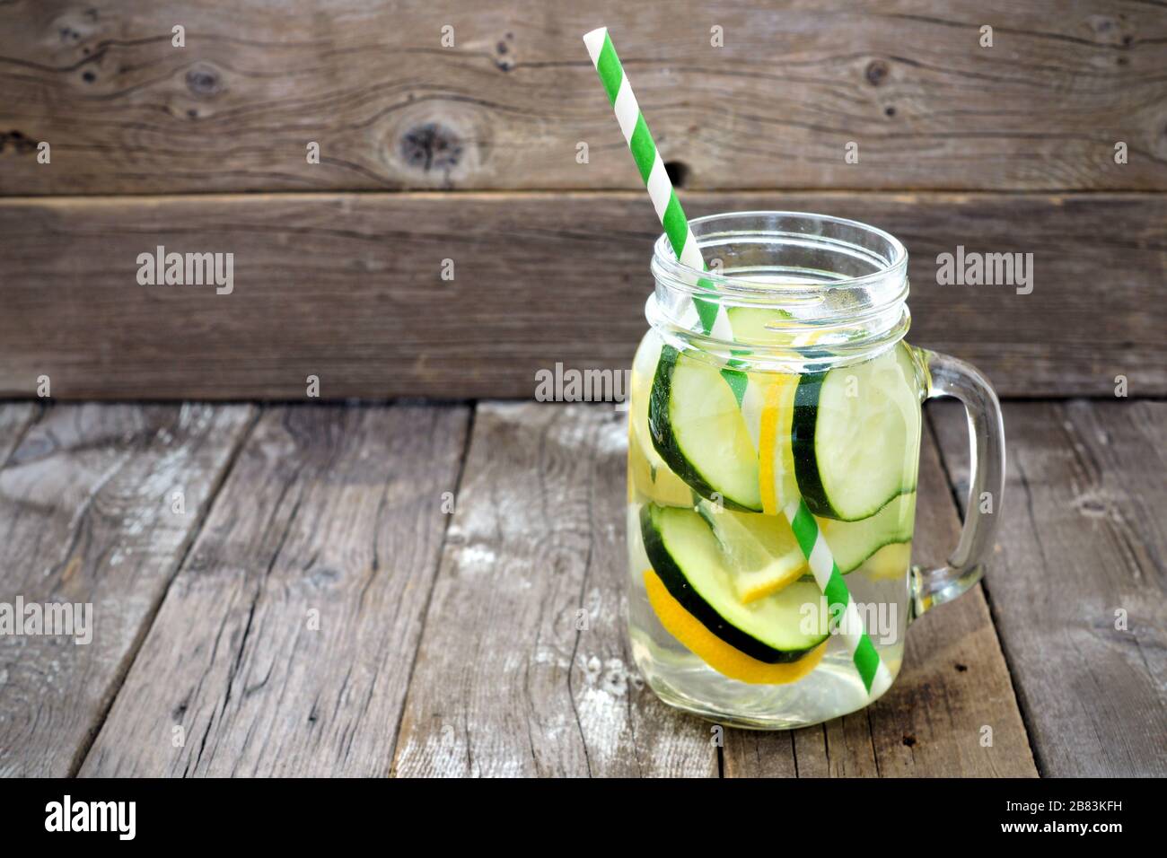 Lemon cucumber detox water in a mason jar glass with straw against a rustic wood background Stock Photo